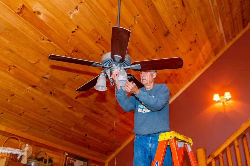 Dave on a ladder installing a ceiling fan in a cabin
